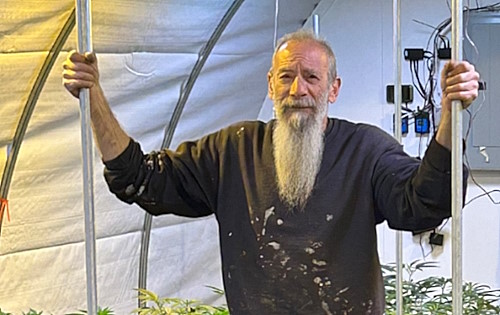 Mark Turkheimer standing in a Mark Turk Farms greenhouse, hands on the hoop frame, cannabis plants in the foreground